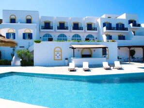 A poolside area with a clear blue pool, white buildings with blue accents, and outdoor seating. - Patmos Paradise Hotel (Patmos)