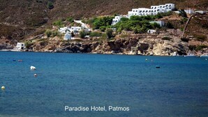 A coastal hotel with white buildings, a clear blue sea, and rocky terrain.