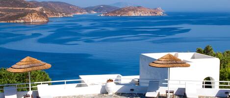 A poolside area with lounge chairs and umbrellas, overlooking a large body of water and distant land.