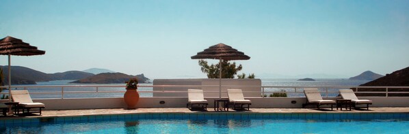 A poolside area with lounge chairs and umbrellas, overlooking a body of water and distant mountains. - Patmos Paradise Hotel (Patmos)