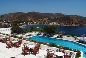 A pool area with lounge chairs and tables, overlooking a bay with boats and a hilly landscape. - Patmos Paradise Hotel (Patmos)