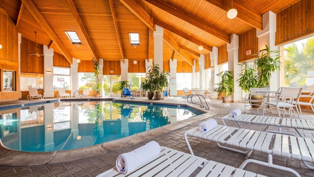 An indoor swimming pool with clear water, surrounded by white lounge chairs and potted plants. - Best Western Plus Corning Inn (Corning)