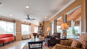 A spacious living room with a ceiling fan, large windows, and a variety of seating options including a red sofa, a brown armchair, and a patterned couch. - Best Western Plus Corning Inn (Corning)