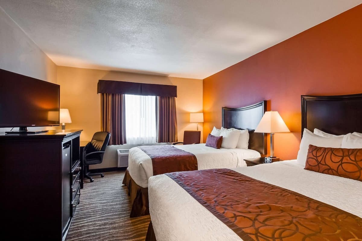 Une chambre d’hôtel avec deux lits, un bureau, une chaise, une télévision et une fenêtre avec des rideaux.