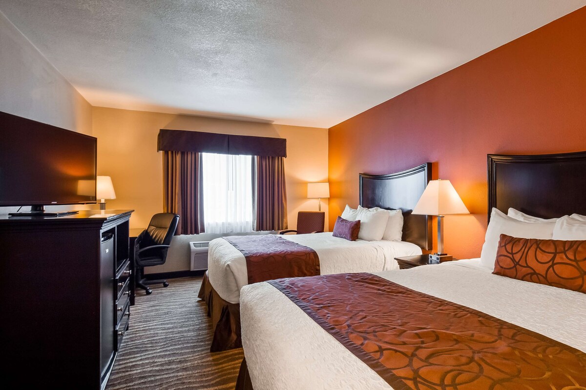 A hotel room with two beds, a desk with a computer, a chair, and a window with curtains.