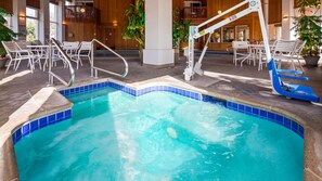 A swimming pool with a blue-tiled edge, surrounded by white chairs and a sun lounger.