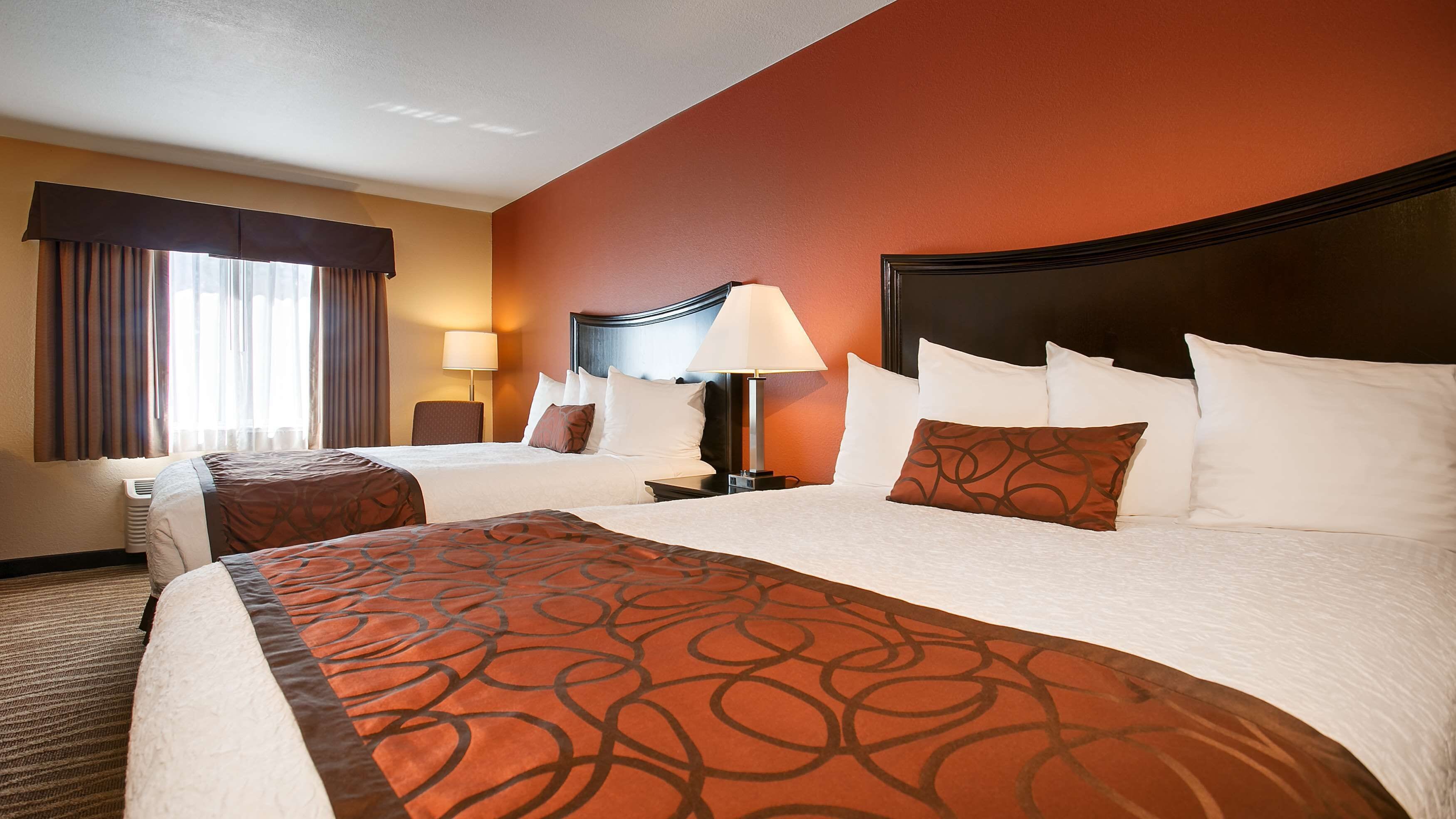 A hotel room with two beds, a nightstand, a lamp, and a chair.