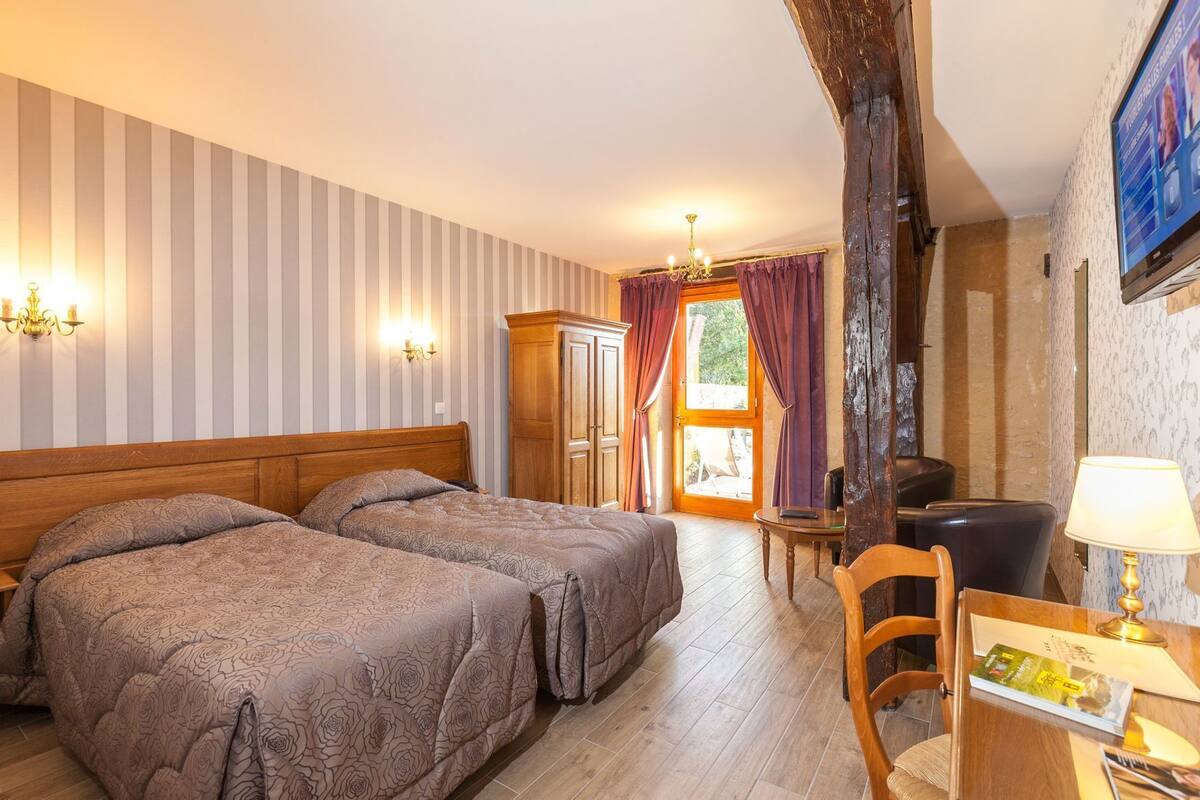 Une chambre d’hôtel avec deux lits, une armoire en bois, un bureau avec une chaise, une lampe et un téléviseur.