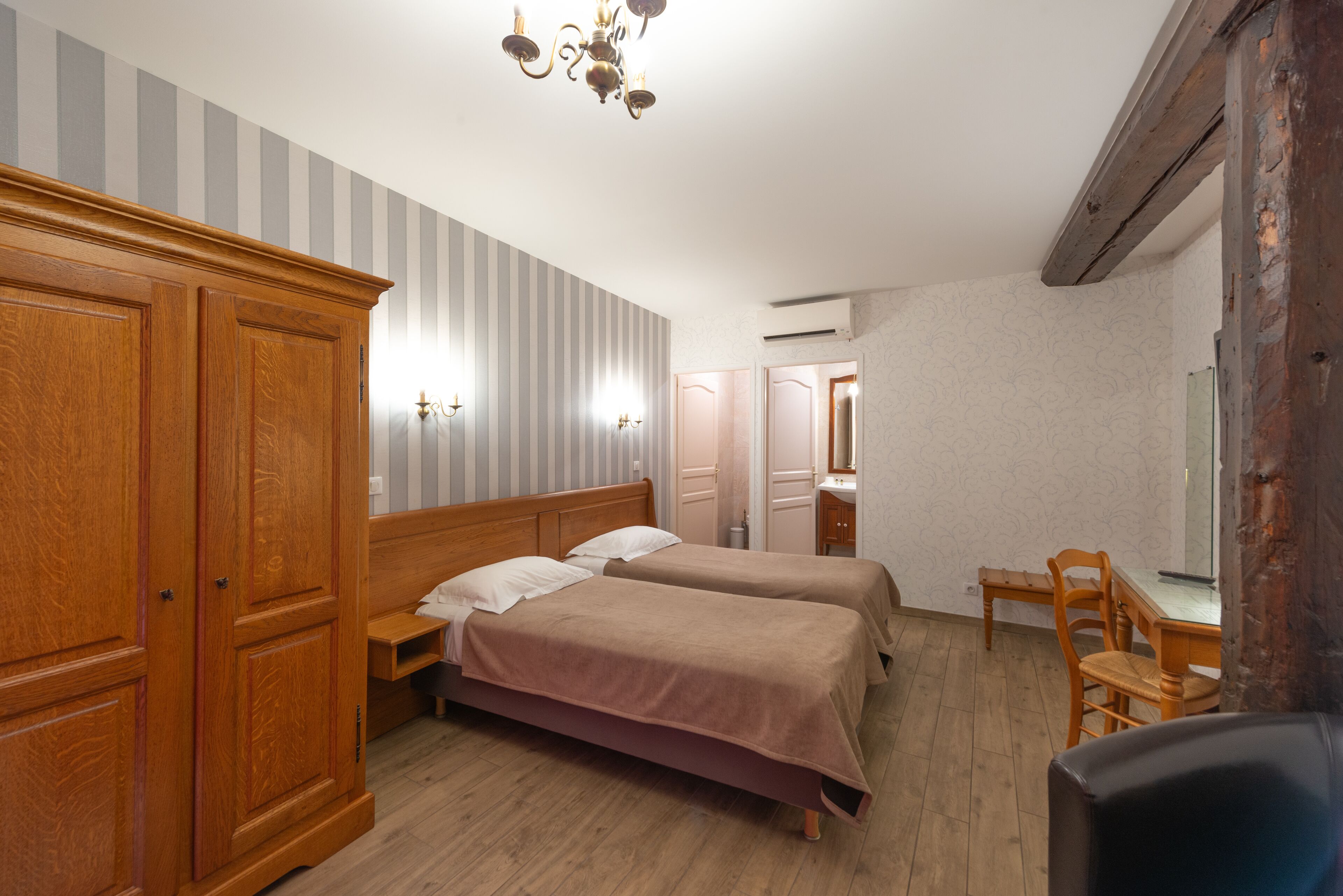 A hotel room with two beds, wooden wardrobe, a desk with a chair, and a mirror.