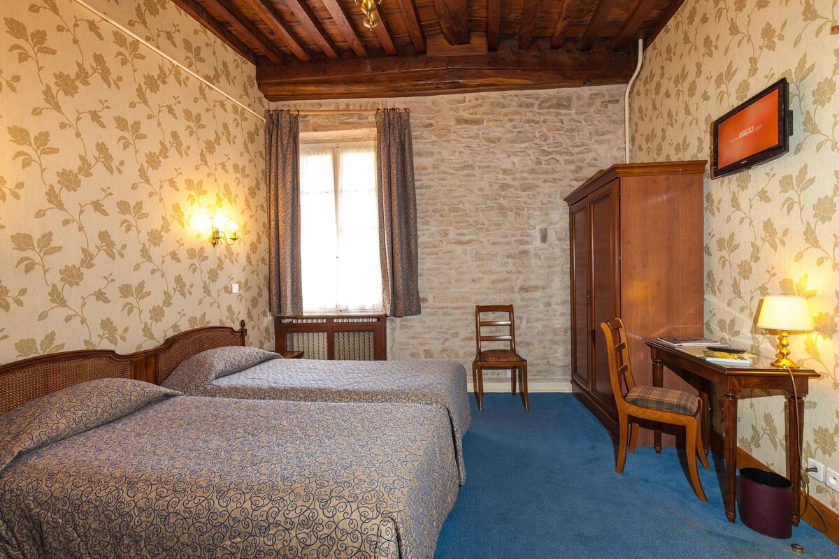 Une chambre avec deux lits, un bureau avec une lampe, une chaise, une armoire et une fenêtre avec des rideaux.