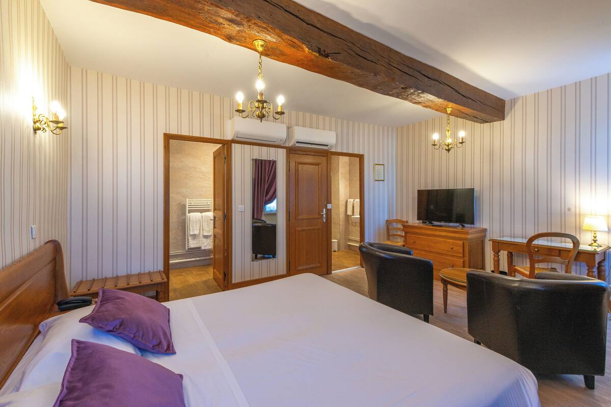 Une chambre d’hôtel avec un grand lit, une tête de lit en bois, un bureau avec une chaise, une télévision et une armoire avec un miroir.