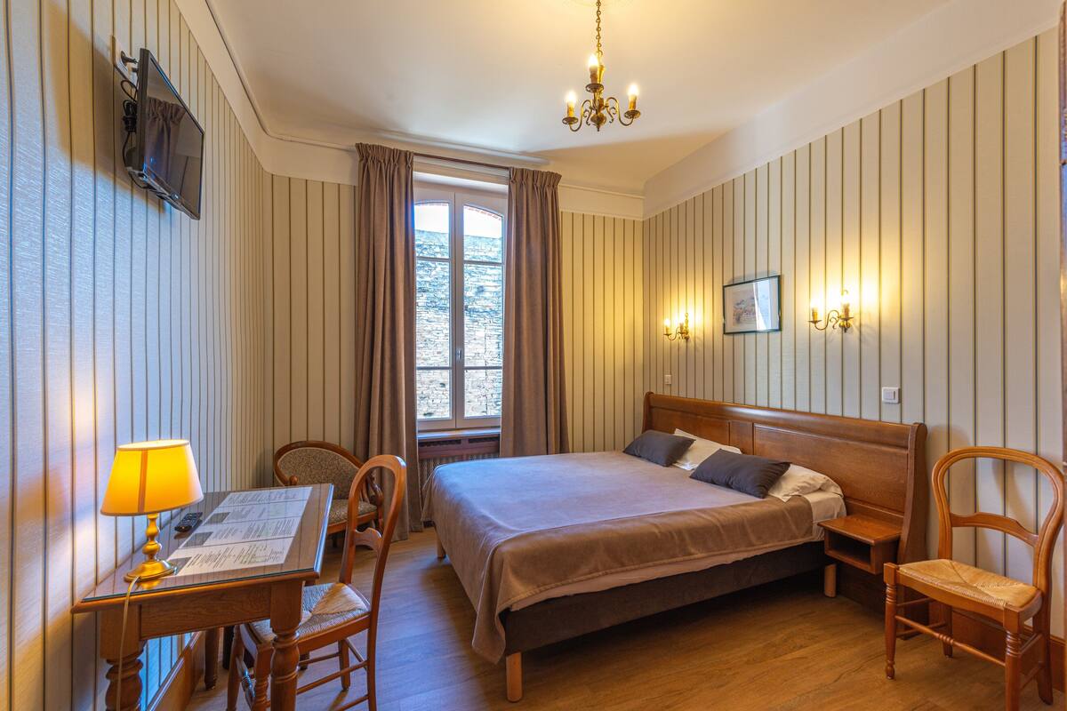 Une chambre d’hôtel comprenant un lit, un bureau avec une lampe, une chaise, un téléviseur fixé au mur et un lustre.