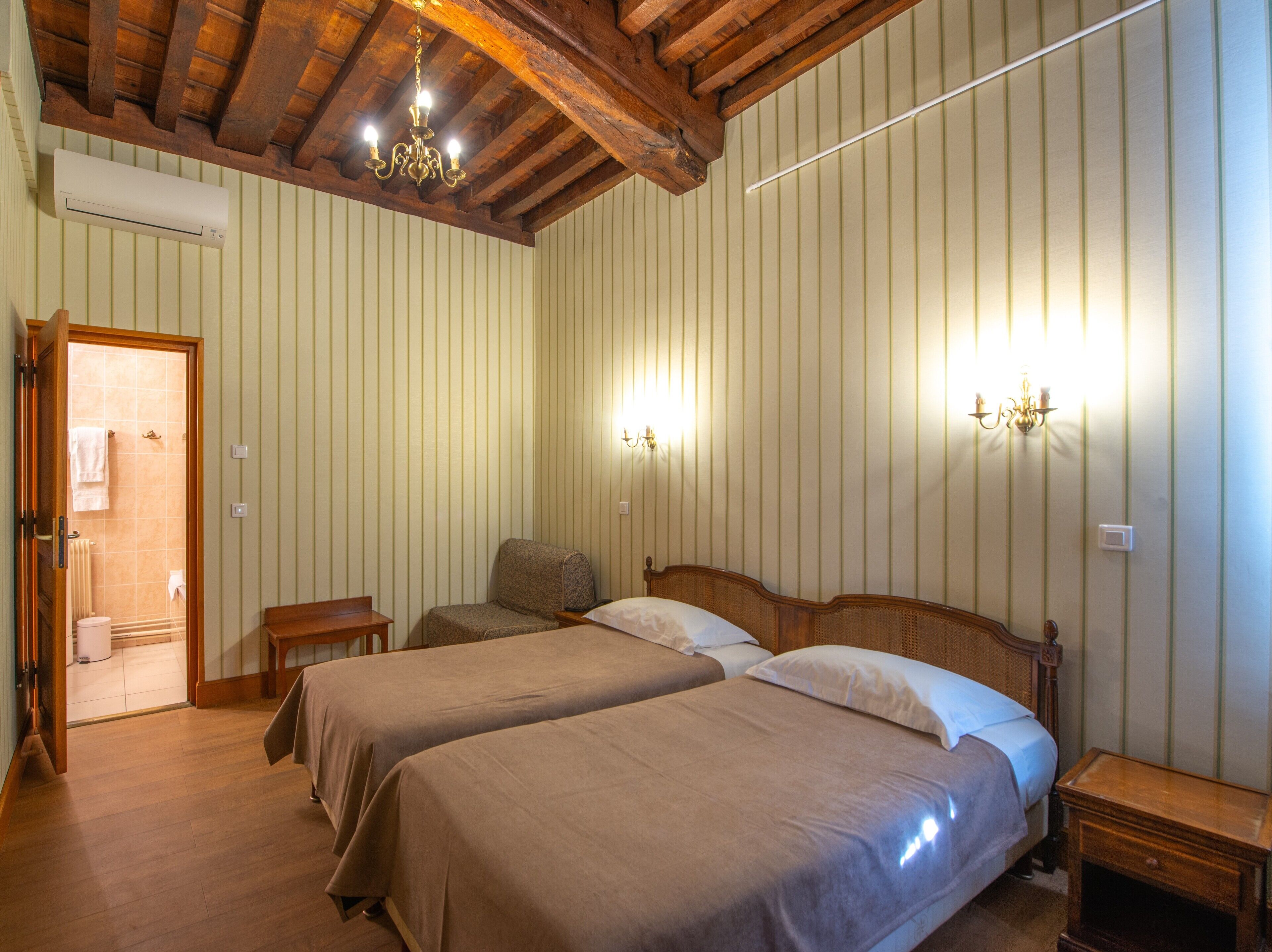 Habitación de hotel con dos camas, vigas de madera en el techo, una araña y apliques de pared.