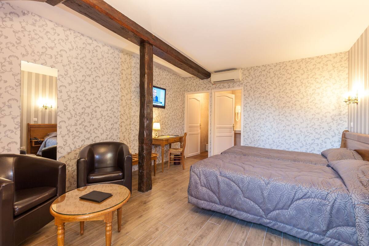 Une chambre d’hôtel comprenant un lit, deux fauteuils en cuir, une petite table, un bureau et un téléviseur.