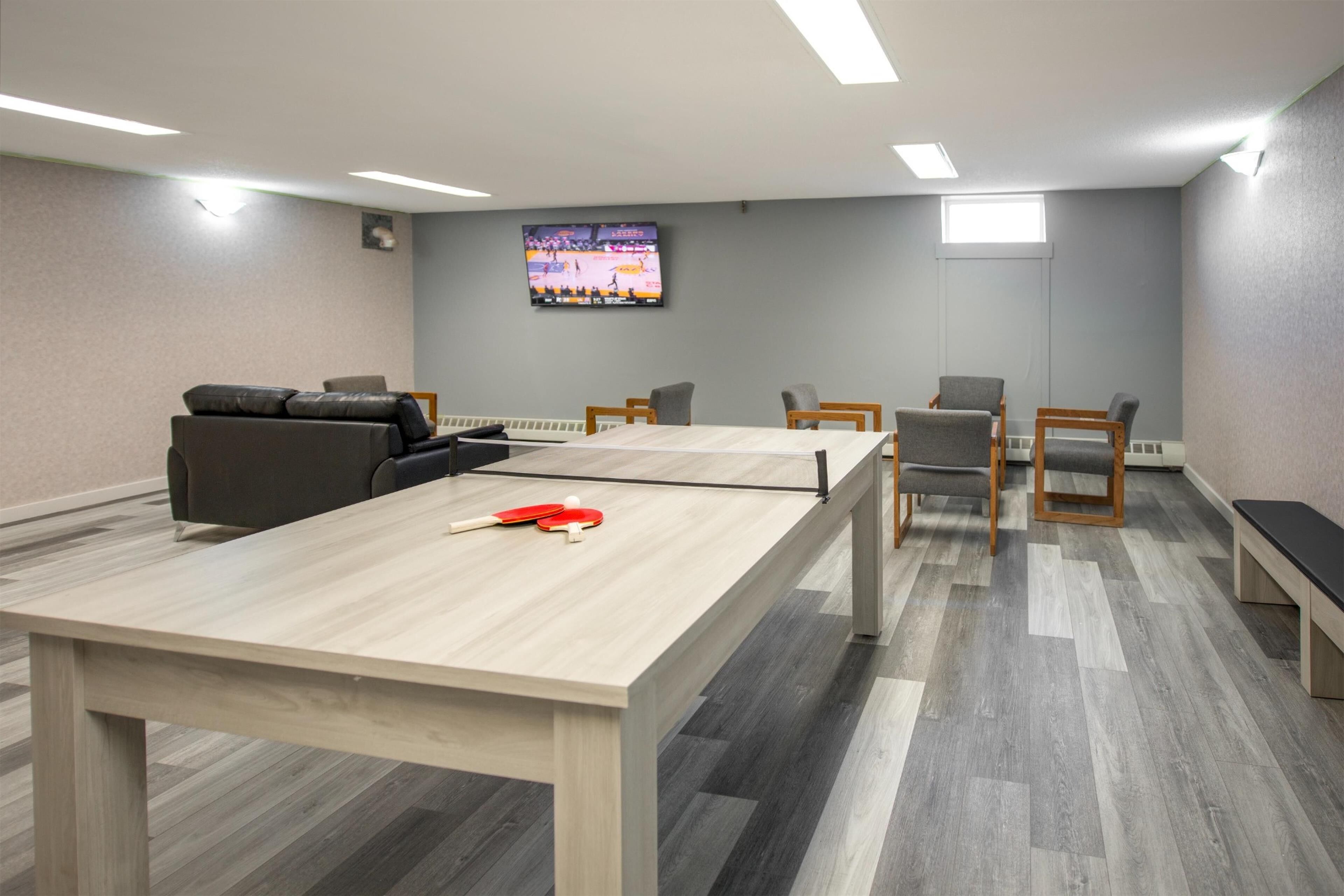A conference room with a ping pong table, chairs, a sofa, and a TV on the wall.