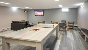 Un salón de conferencias con una mesa de ping pong, sillas, un sofá y un televisor en la pared.