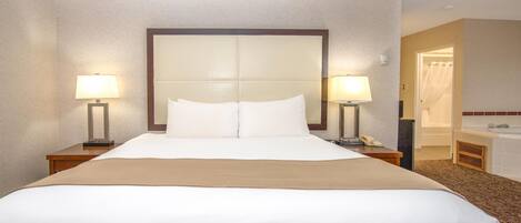 A hotel room with a large bed, two bedside lamps, a nightstand, a mirror, and a bathroom visible through an open door.
