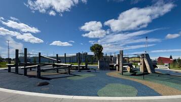 A playground with various play structures, including a slide and climbing frames, set on a blue and green rubberized surface.