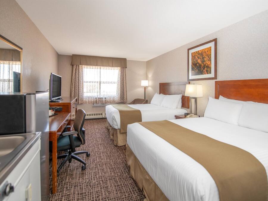 Une chambre d’hôtel avec deux lits, un bureau avec un ordinateur, une télévision et une fenêtre avec des rideaux.