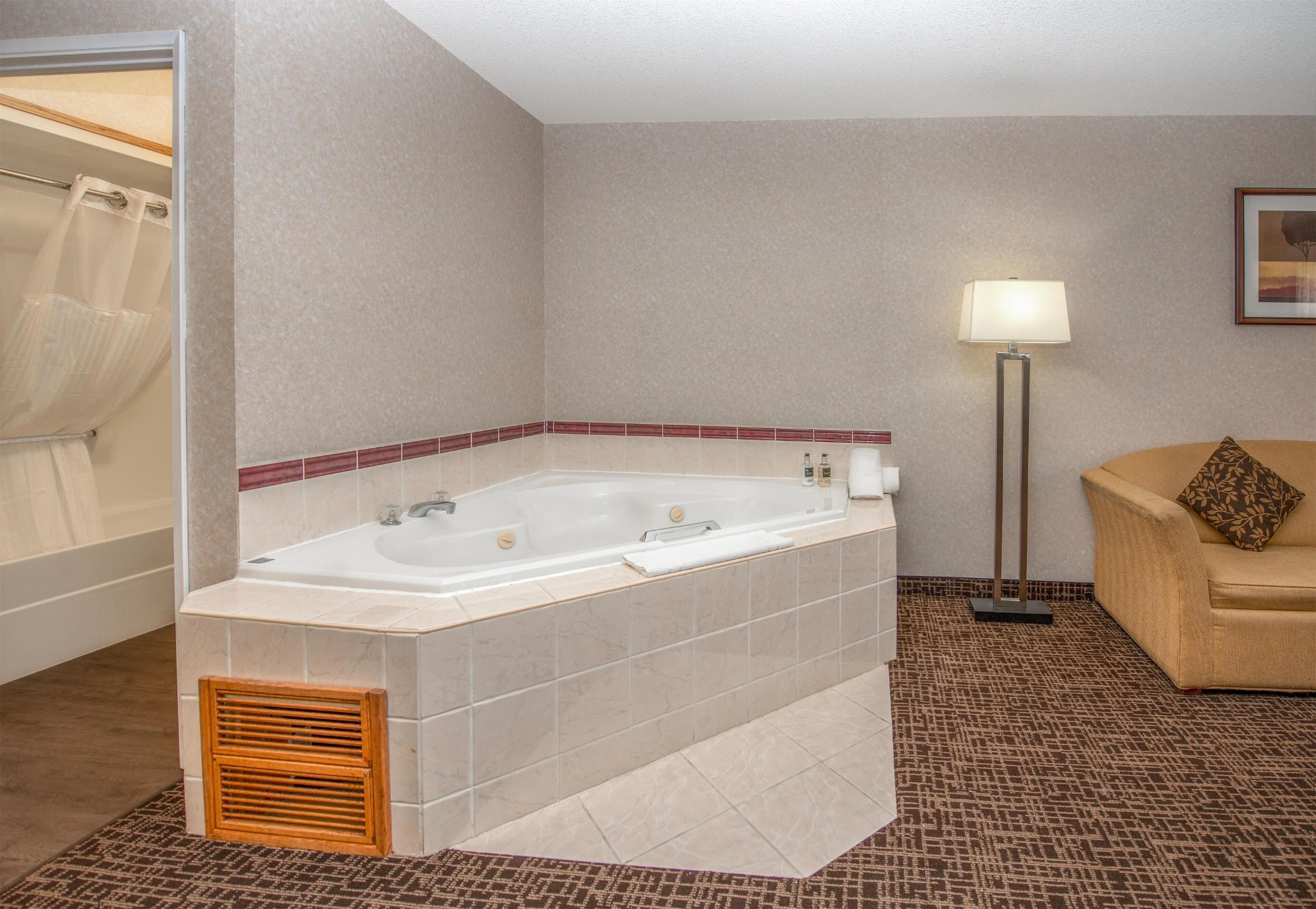 Une salle de bain avec une grande baignoire, une douche, un lampadaire et un canapé avec un coussin.