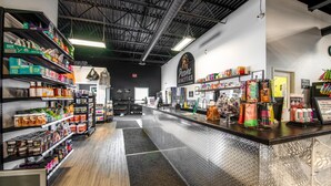 Interior de una tienda minorista con estantes llenos de diversos productos, un mostrador con artículos a la venta y un logotipo en la pared.