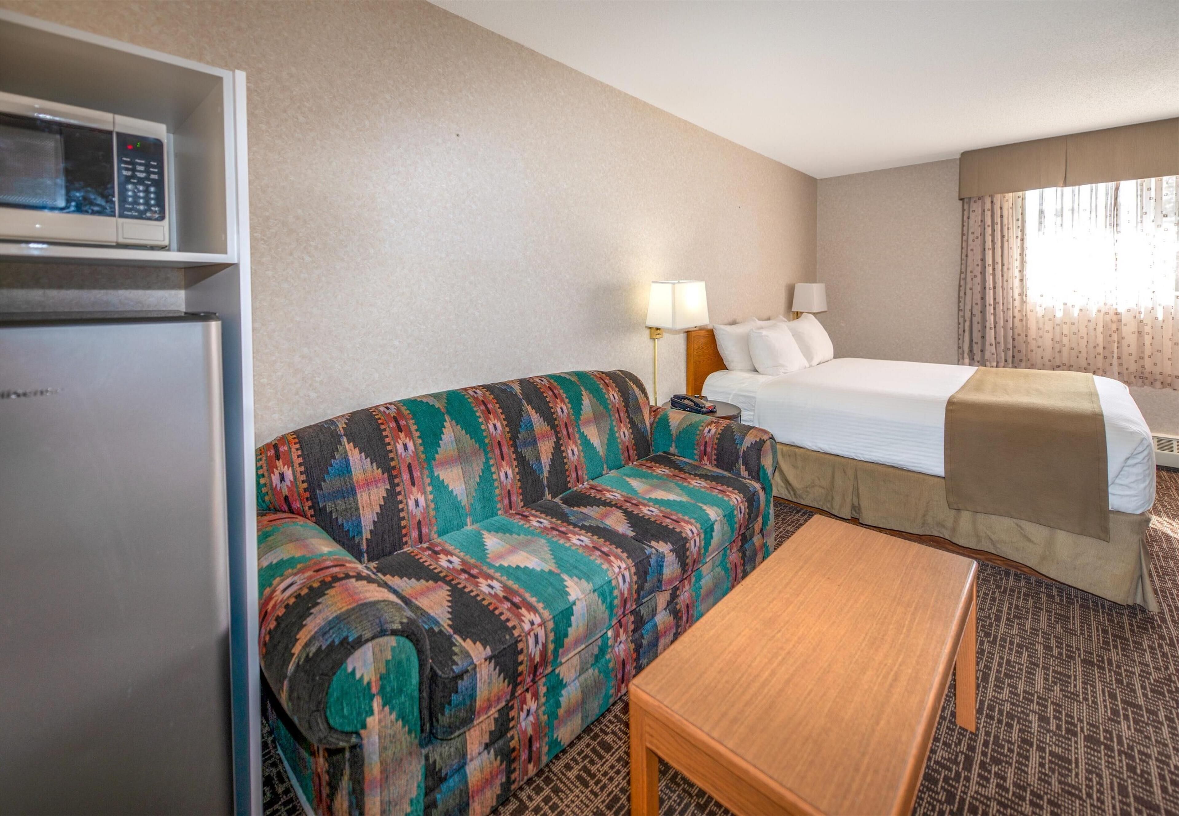 Een hotelkamer met een bed, een bank, een tafel, een magnetron en een koelkast.