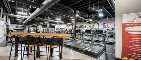Un gimnasio con cintas de correr, una mesa de madera con sillas y un letrero sobre PRISM LIGHT.