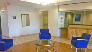 A lobby with blue chairs, a glass coffee table, a reception desk, and an exit sign. - Motel 6 Rocky Mount, NC (Rocky Mount)