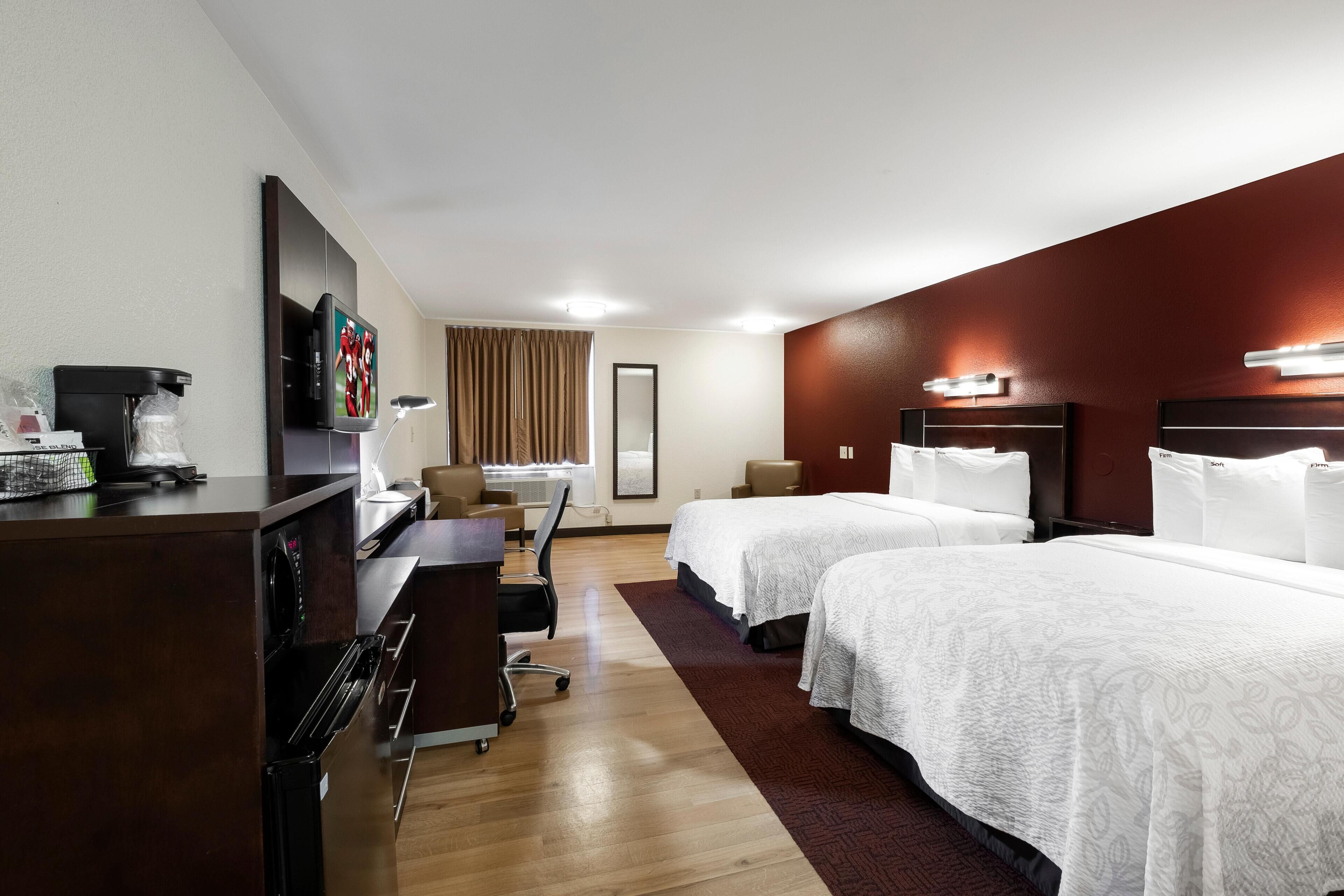 A hotel room with two beds, a desk with a computer, a coffee machine, and a TV.
