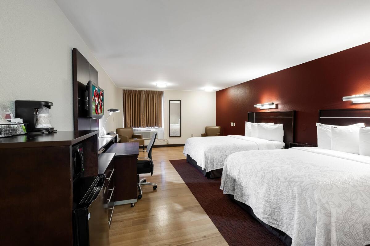 A hotel room with two beds, a desk with a computer, a coffee machine, and a TV.