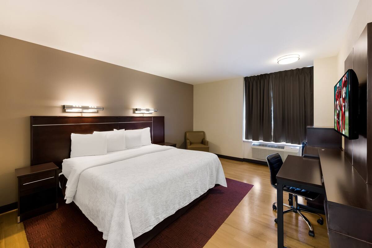 A hotel room with a large bed, a desk, a chair, a TV, and a window with curtains.