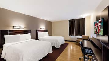 A hotel room with two beds, a desk, a chair, a television, and a window with curtains.