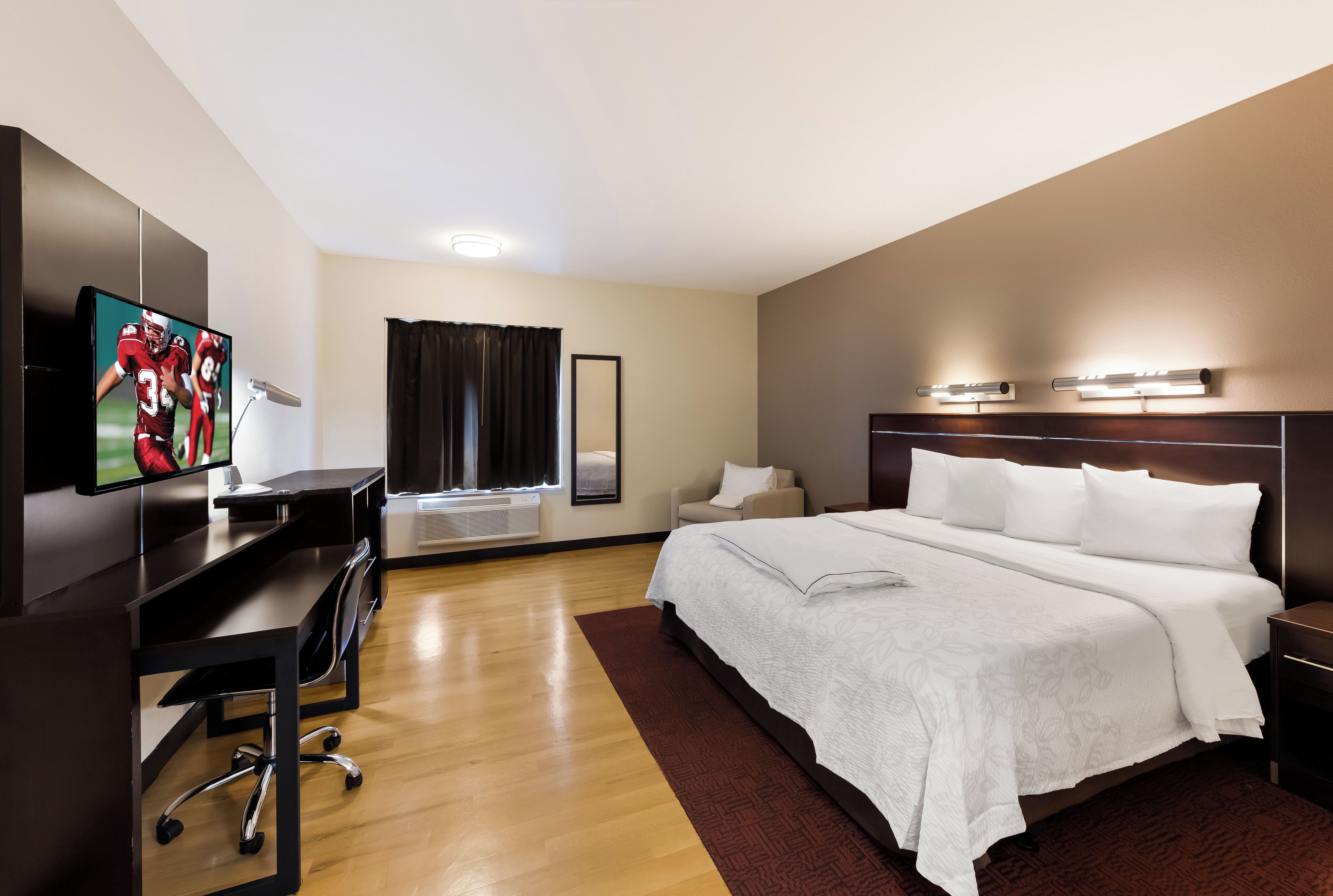 Una habitación de hotel con cama, escritorio, televisión y ventana con cortinas.
