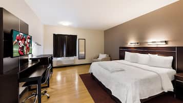 Una habitación de hotel con cama, escritorio, televisión y ventana con cortinas.
