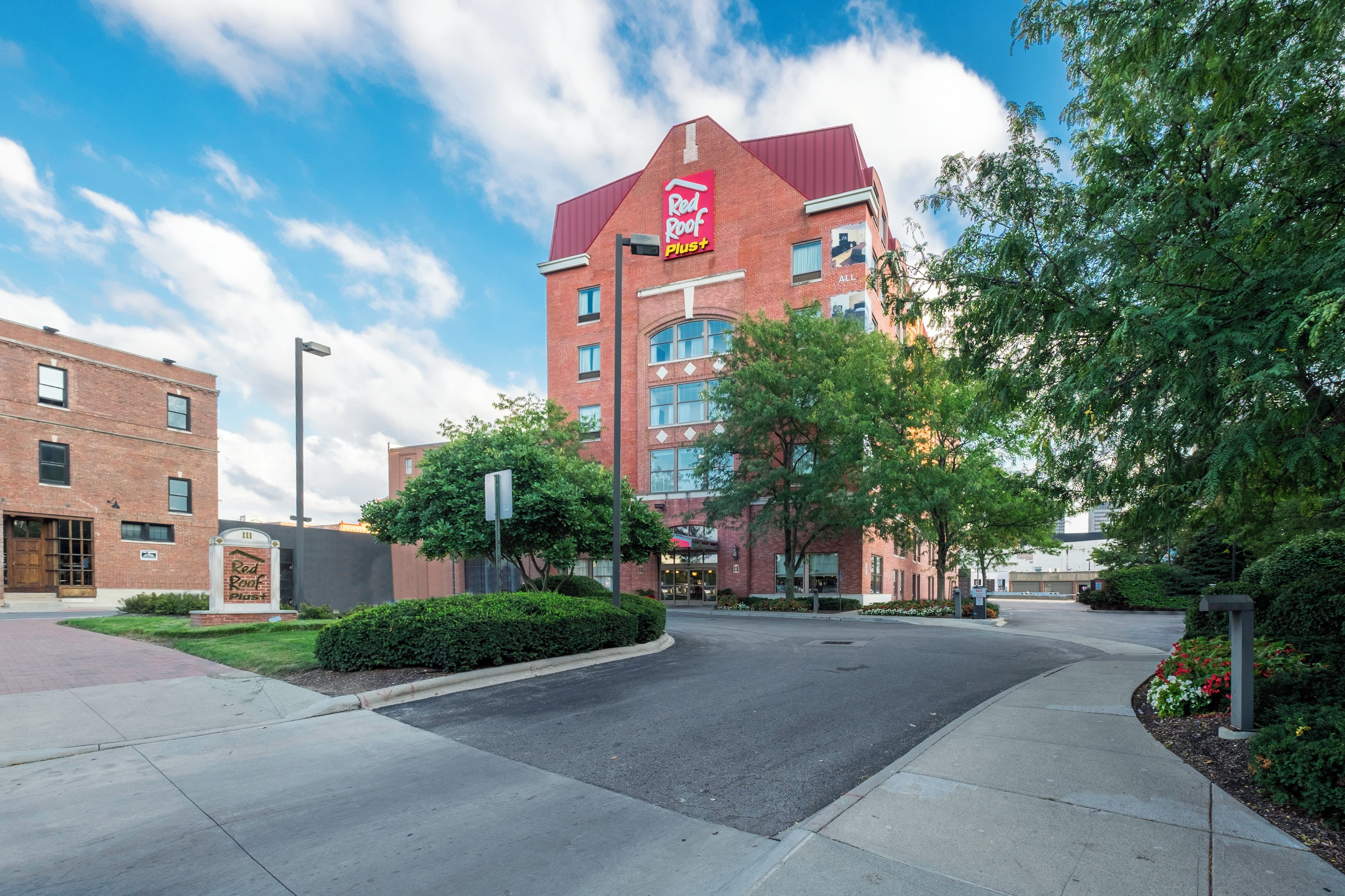 A Red Roof Plus hotel with a brick facade, multiple windows, and a clear sky.
