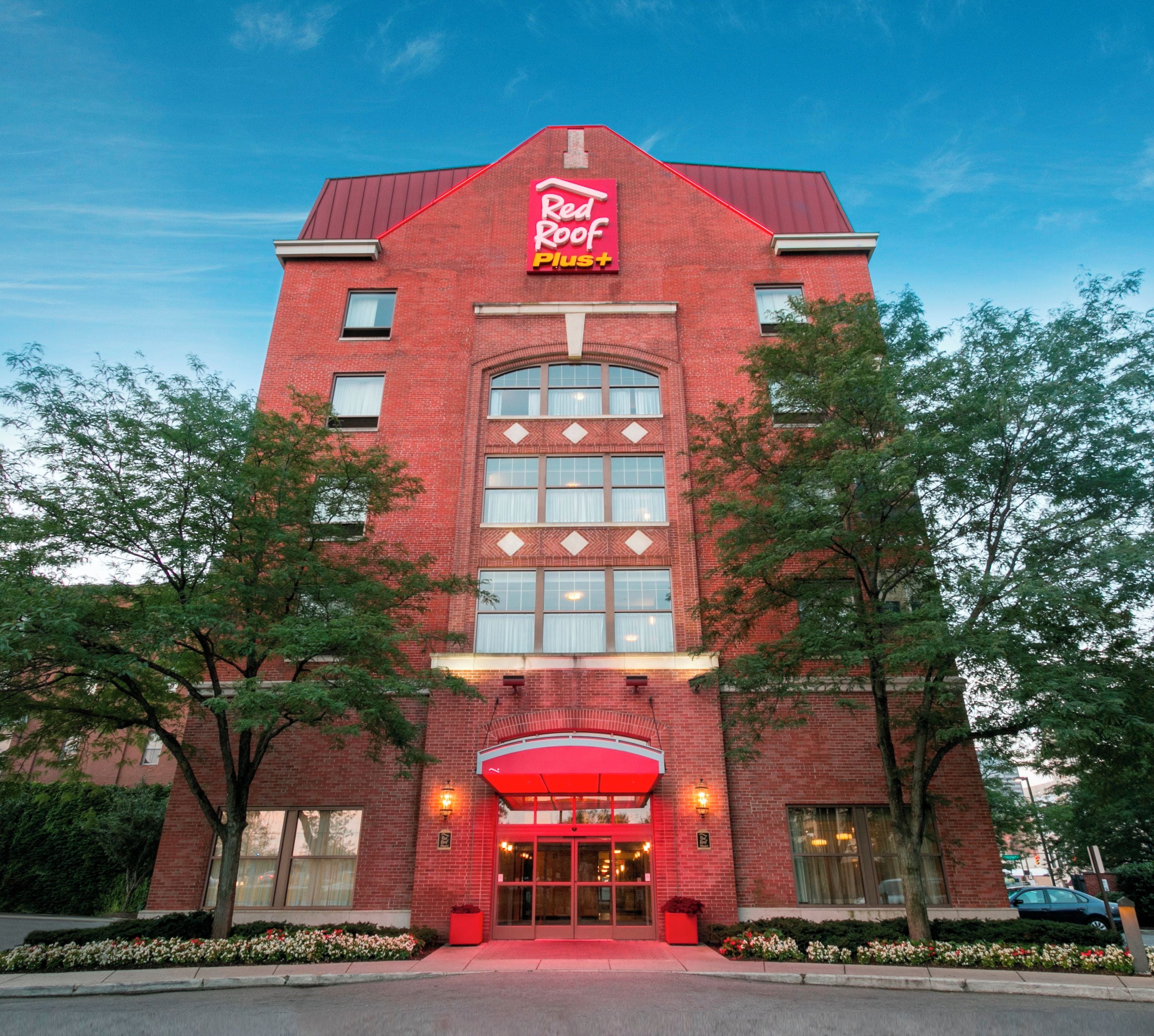 A Red Roof Inn Plus hotel with a brick facade, large windows, and a red awning.