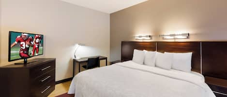 Una camera d'albergo con un letto, una scrivania con lampada, una televisione e una testiera illuminata.
