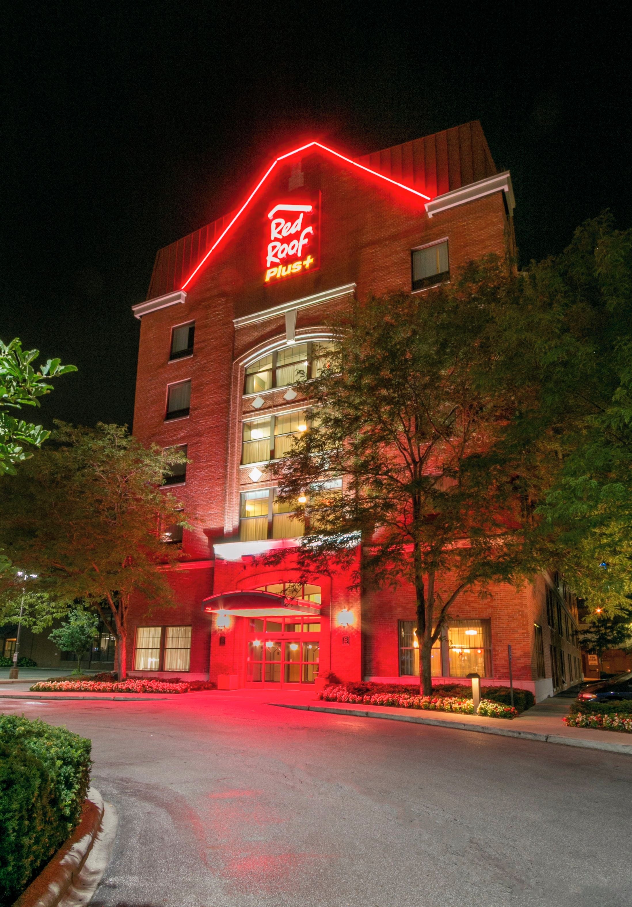 A hotel with a red neon sign, a brick facade, and a modern entrance.
