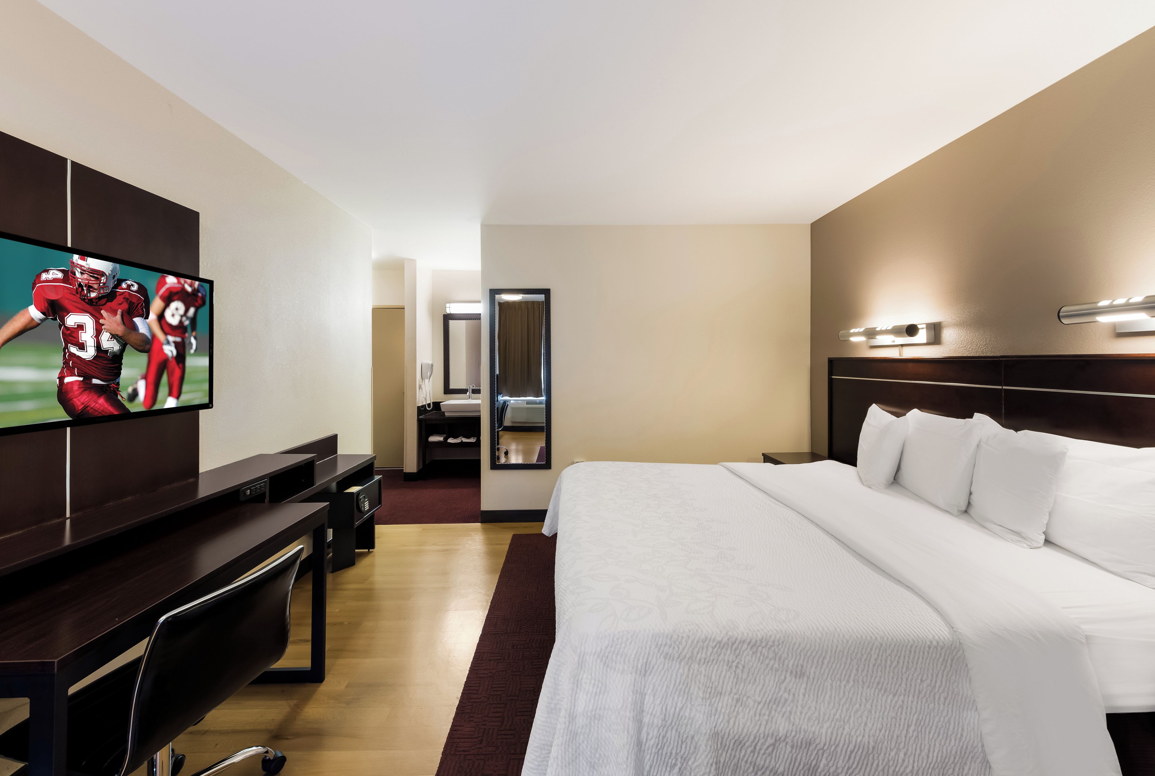 A hotel room with a large bed, a TV mounted on the wall, a desk, and a mirror.