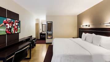 Een hotelkamer met een groot bed, een aan de muur bevestigde televisie, een bureau en een spiegel.