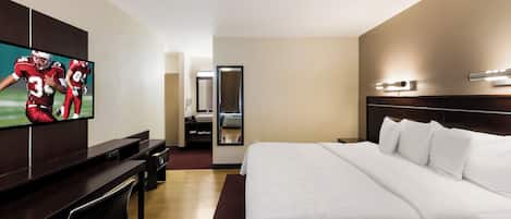 A hotel room with a large bed, a TV mounted on the wall, a desk, and a mirror.