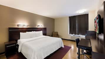 A hotel room with a large bed, bedside tables, a desk with a chair, a flat-screen TV, and a window with curtains.
