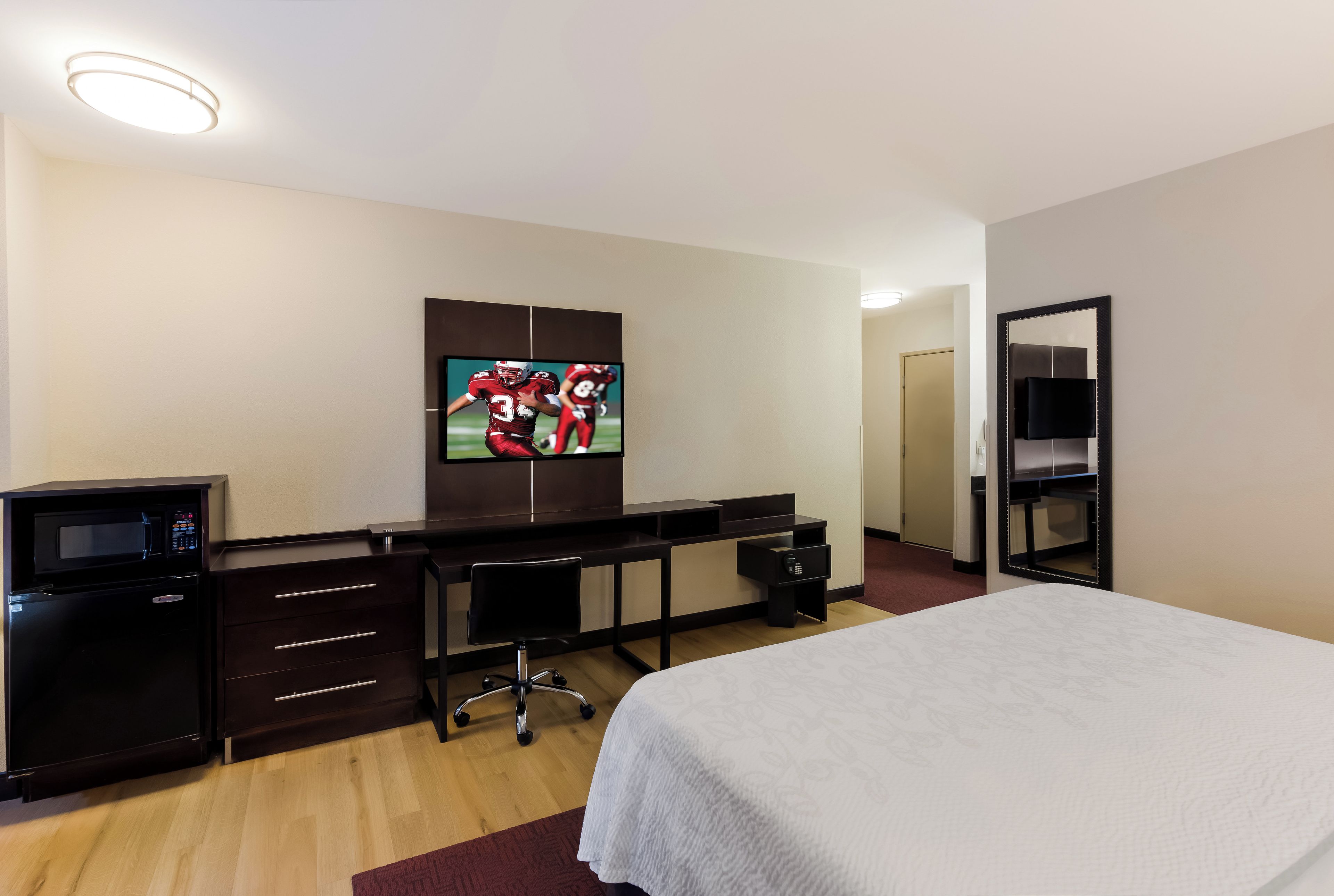 A hotel room with a bed, a desk with a computer, a television, a microwave, and a wardrobe.