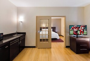 A hotel room with a kitchenette, a bed, a television, and a door leading to another room. - Red Roof Inn PLUS+ Columbus Downtown-Convention Center (Columbus)