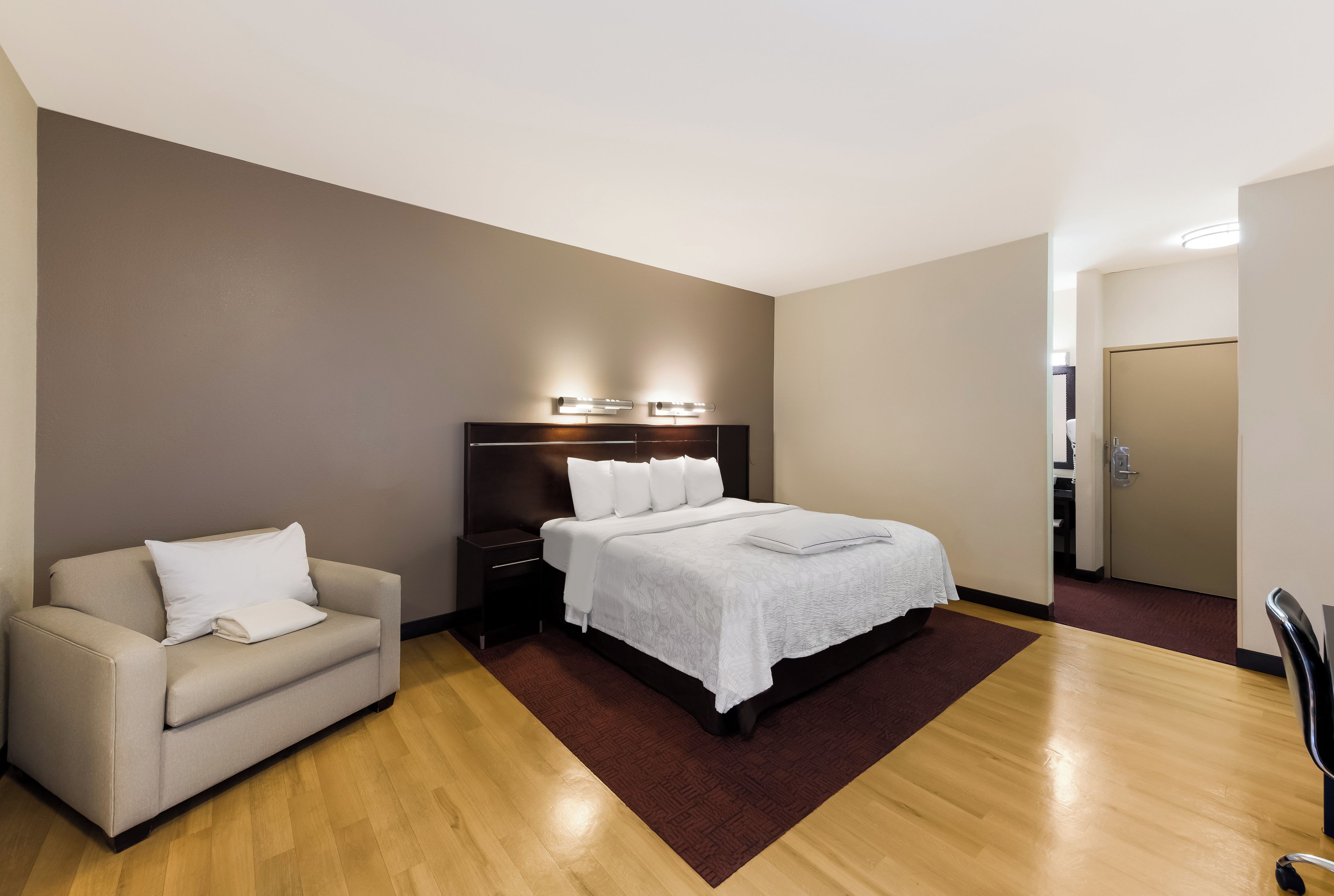 Hotellihuone, jossa on sänky, yöpöytä, tuoli ja vaatekaappi.