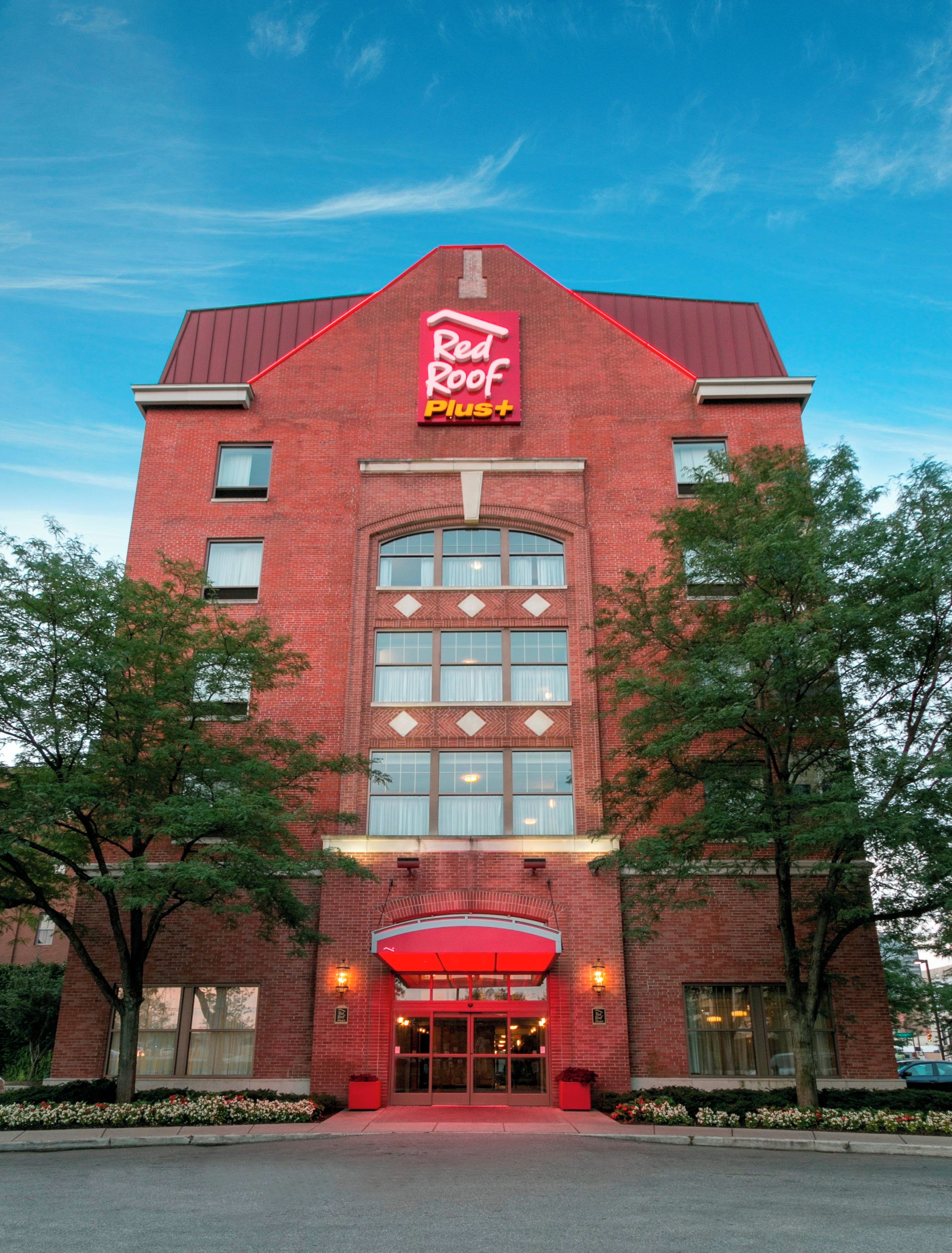 A Red Roof Plus hotel with a brick facade, large windows, and a red awning over the entrance.