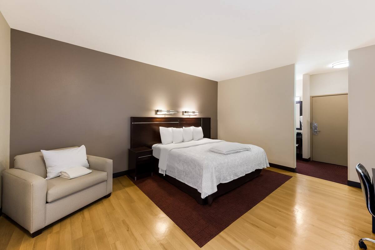 A modern hotel room with a large bed, a sofa, a nightstand, and a wooden floor.