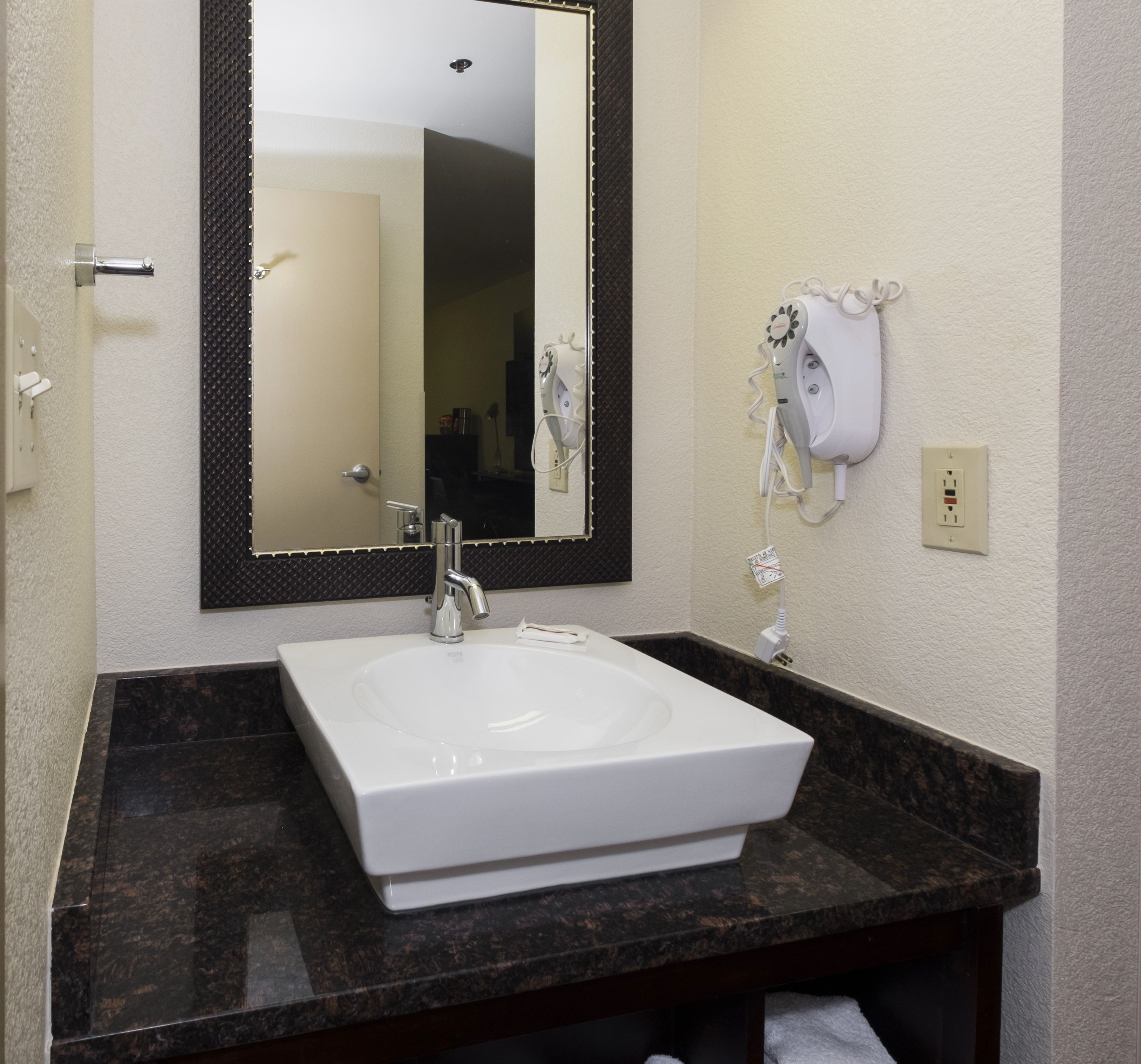 A bathroom with a white sink, a mirror, and a hairdryer on the wall.