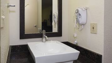 A bathroom with a white sink, a mirror, and a hairdryer on the wall.