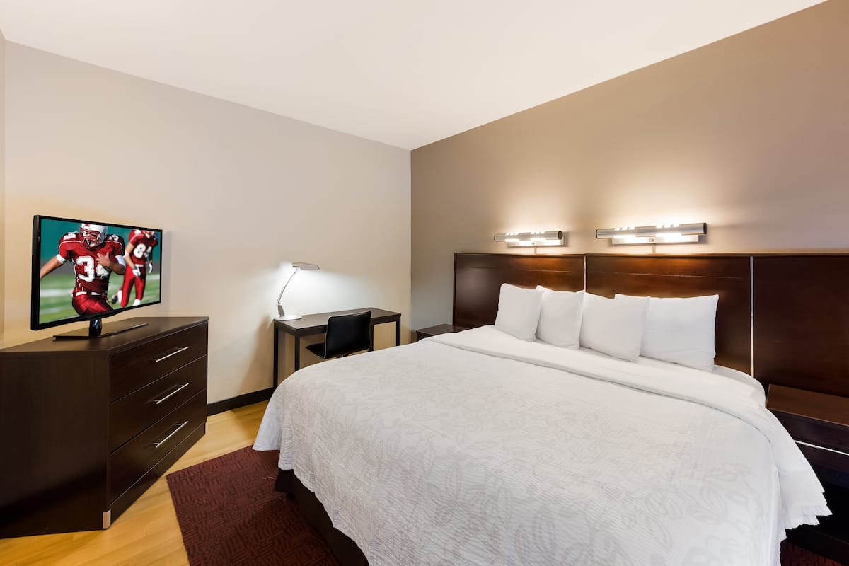 A hotel room with a large bed, a desk with a chair, a TV, and a nightstand.